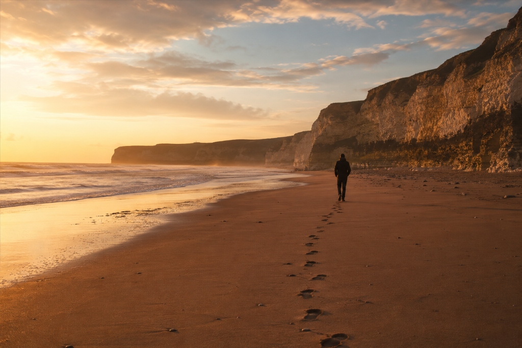 Footsteps in the sand on the Yorkshire coast at golden hour — a lone figure walking toward Flamborough Head