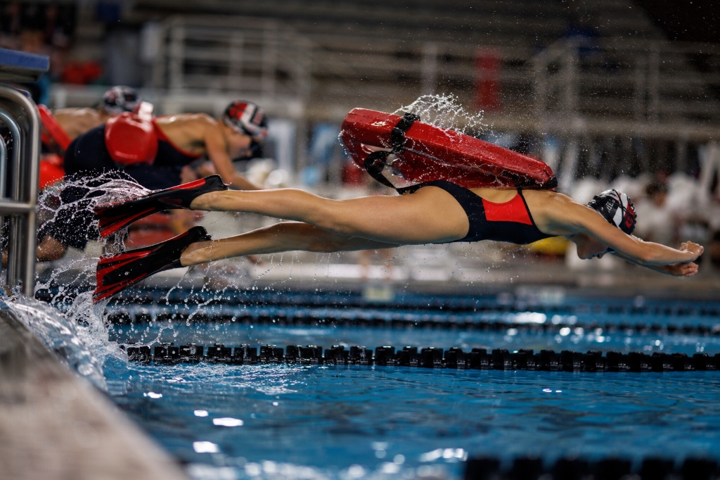 Young lifesaving sport athletes poolside — rescue tube, fins and kickboard, one entering the pool